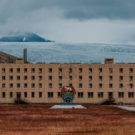 Edificio de la era soviética con emblema en Pyramiden, Svalbard, con telón de fondo glaciar