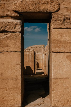 Ancient doorway leading through stone ruins in Saqqara, Egypt under clear skies