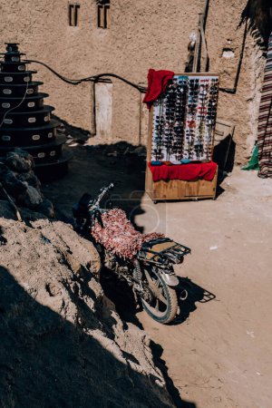 Téléchargez les photos : Motorcycle covered in textiles parked beside a sunglasses stall in Siwa Oasis, Egypt - en image libre de droit