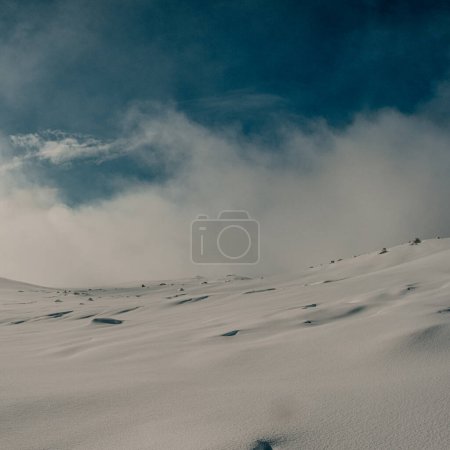 Eine ruhige Winterlandschaft in Myrdalsjokull, Island, mit einem riesigen, schneebedeckten Gelände unter einem klaren blauen Himmel mit wehenden Wolken.