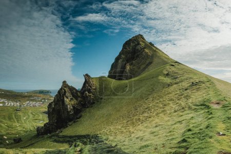 A breathtaking view of the rugged terrain and steep cliffs in the Vestmannaeyjar  (Westman Islands), Iceland, with lush green hills and a dramatic sky. 