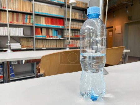 Half-Full Plastic Water Bottle on a Library Table With Bookshelves in the Background.
