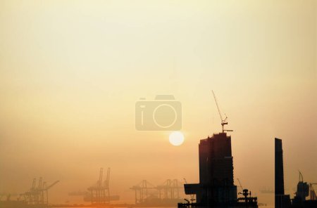 über den Turmdrehkran auf dem Gebäude installiert und hinter sind der Hafen und die Logistik unter Sonnenuntergang