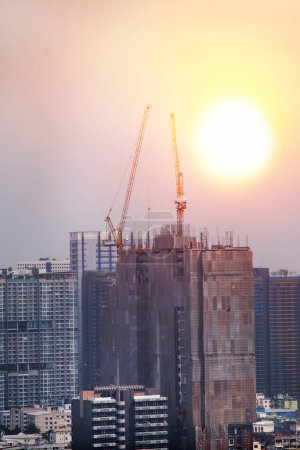 about a twin tower crane at the construction building working through sunset