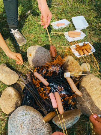 Photo for Campsite with friend. Cooking fried sausages and marshmallow on a fire in the forest. - Royalty Free Image