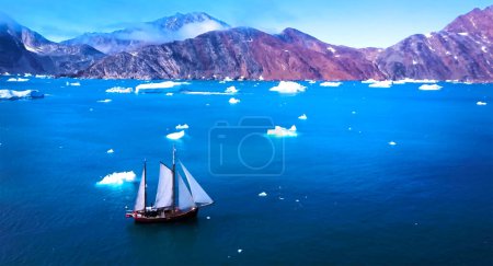 Imagen de gran angular de un barco solitario en medio del Océano Ártico con pequeños icebergs flotantes y montañas al fondo.