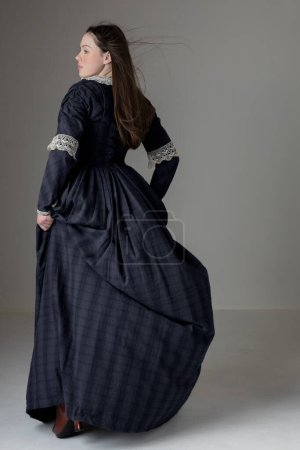 Eine junge viktorianische Frau trägt vor Studiokulisse ein blaues Baumwollkleid mit Spitzenbesatz
