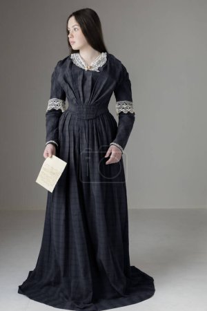 Eine junge viktorianische Frau trägt ein blaues Baumwollkleid mit Spitzenbesatz und hält einen Brief vor einer Studiokulisse