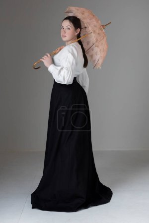 Téléchargez les photos : Une jeune femme victorienne ou édouardienne portant un chemisier Garibaldi en lin blanc et une jupe noire et tenant un parasol vintage - en image libre de droit