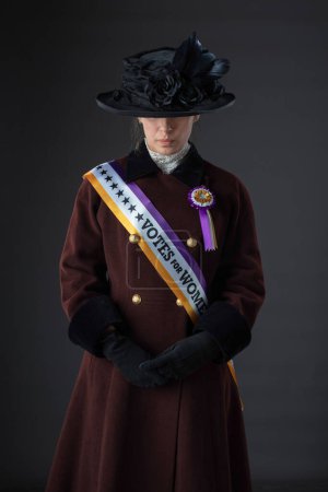 American Victorian or Edwardian Suffragette wearing historically accurate sash and rosette and protesting for women's voting rights against a studio backdrop