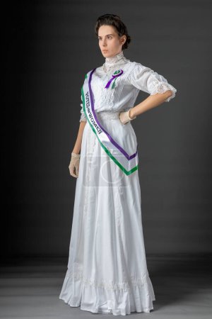 United Kingdom Victorian or Edwardian Suffragette wearing historically accurate purple and green sash and rosette and protesting for women's voting rights against a studio backdrop