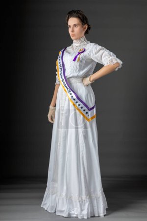 Sufragista estadounidense victoriana o eduardiana vestida con un marco y una roseta históricamente precisos y protestando por los derechos de voto de las mujeres contra un telón de fondo de estudio
