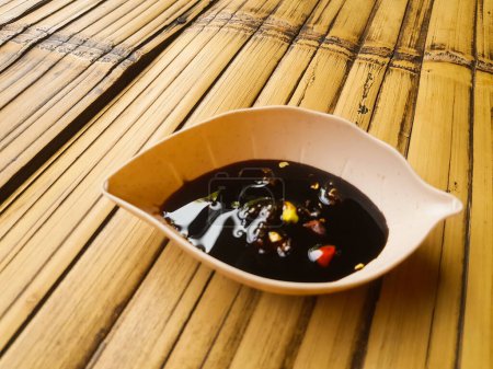 A bowl of soy sauce with chili peppers on a bamboo mat