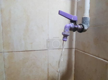 A purple faucet with water flowing, mounted on a beige tiled wall