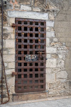 Eine alte rostige Eisentür, die in einer Steinmauer durchrostet.