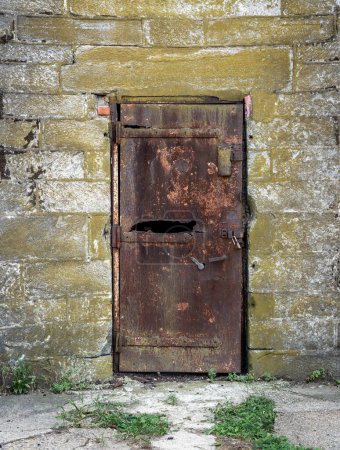 Eine alte rostige Eisentür, die in einer Steinmauer durchrostet.