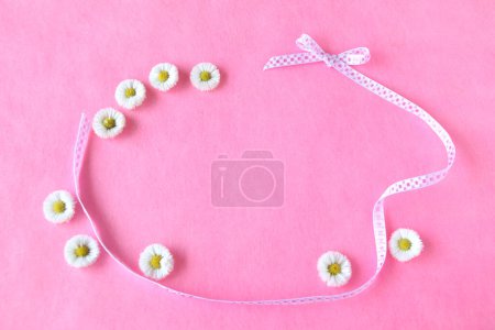 beautiful flowers on a pink background. top view. ribbon and daisy frame 