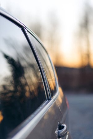 Autoscheibe eines grauen Autos reflektiert Sonnenuntergang und Wald in Norwegen