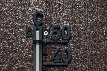 Primer plano de la parte superior de un termómetro negro colgado en una pared de madera marrón, termómetro celcius que muestra 40 y 50. Montañas noruegas.