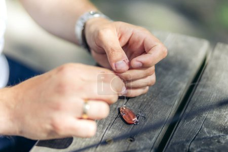 Closeup of hands tying a fishing knot on a fishing lure on a wooden table in sunshine. Summer in Norway.