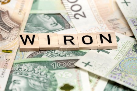 Close-up view of Scrabble tiles spelling 'WIRON' set against a colorful backdrop of various international and Polish currency notes.