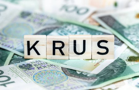 Gros plan de lettres de scrabble en bois orthographiant "KRUS" au sommet d'une pile de zlotys polonais, capturant des concepts financiers ou économiques.