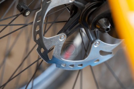 Detailaufnahme der Scheibenbremse eines Fahrrads mit Rotor, Bremssattel und Speichen auf gelbem Rahmen. Perfekt für Fahrradausrüstung und Wartungsinhalte.