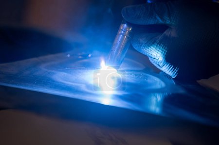Captured in dim lighting, this image features a welder wearing a glove while skillfully operating a welding torch. Blue sparks fly off the metal surface during the welding process.