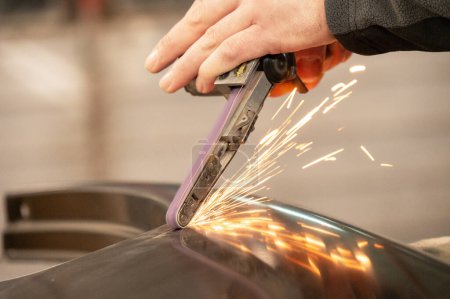 A skilled worker grinds the edge of a metal sheet using a hand-held grinding machine, creating a bright stream of sparks in an industrial environment.