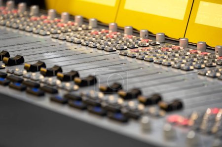 Gros plan détaillé d'une console de mixage audio professionnelle avec de nombreux boutons de commande, curseurs et sections à code couleur. Focus sur les équipements d'ingénierie du son en studio.