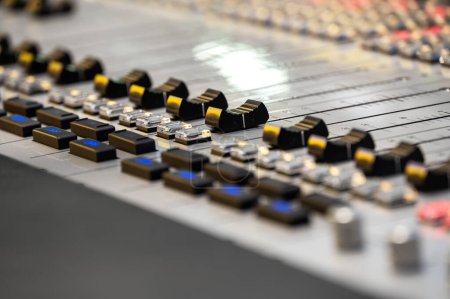 Detailed close-up of a professional audio mixing console used in sound recording and production. The focus is on the intricately designed sliders and knobs.