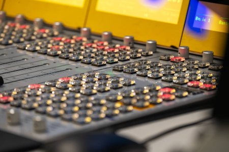 A detailed close-up captures the complex interface of a professional audio mixing console with illuminated buttons and sliders, essential in a music production environment.