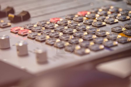A close-up view of a professional audio mixing console with illuminated buttons and dials, highlighting the technology used in sound engineering and music production.