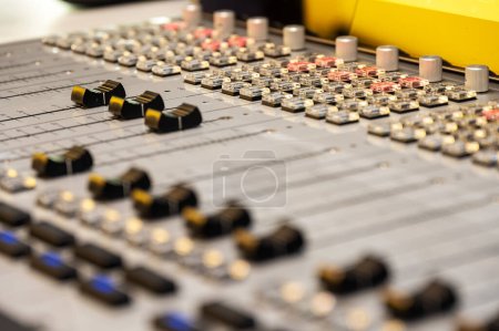 Primer plano detallado de una consola de mezcla de audio profesional en un estudio de grabación, destacando la variedad de faders, botones y botones de control utilizados para ajustar los niveles de sonido.