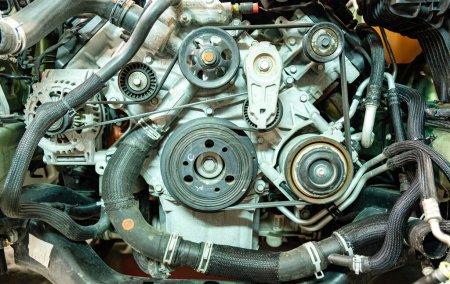 Image rapprochée d'un moteur de voiture complexe détaillant l'assemblage de courroies, de poulies et d'autres pièces mécaniques, généralement présentes dans le compartiment moteur d'un véhicule.