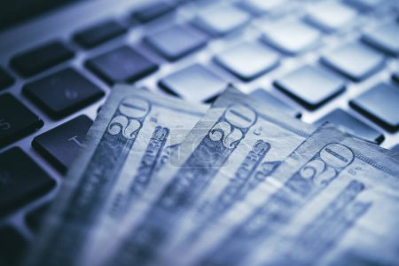 Eine Nahaufnahme erfasst amerikanische 20-Dollar-Scheine, die auf einer modernen Laptop-Tastatur angeordnet sind und Themen wie Online-Finanztransaktionen und digitales Währungsmanagement betonen..