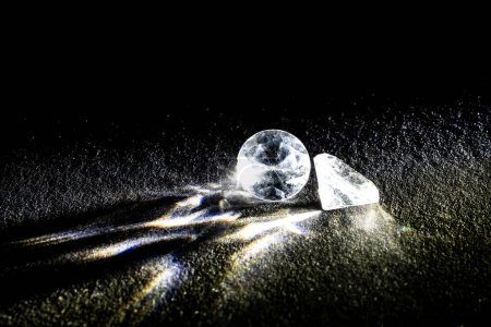 Deux diamants taille brillant reposant sur une surface sombre et texturée, scintillant sous un faisceau de lumière, illustrant l'opulence et les goûts individuels de haute valeur nette.