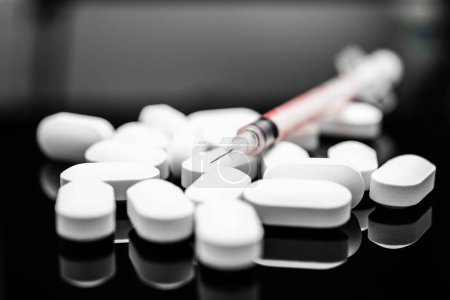 Ein beeindruckendes Bild, das eine Sammlung weißer Pillen neben einer Spritze vor einem reflektierenden schwarzen Hintergrund festhält und Themen wie medizinische Behandlung und Gesundheitsinterventionen, Drogenabhängigkeit, Fentanyl darstellt.