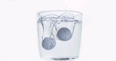 Photo for Tablets Falling and Dissolving into a Glass of Water against White Background - Royalty Free Image