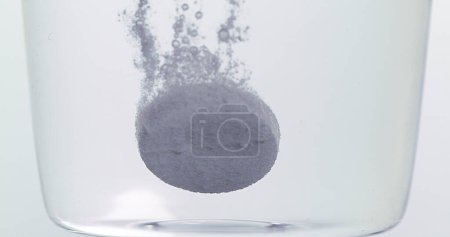 Photo for Tablets Falling and Dissolving into a Glass of Water against White Background - Royalty Free Image