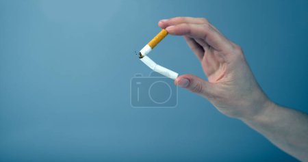 Photo for Hand breaking a cigarette against blue background - Royalty Free Image