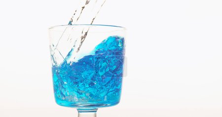Foto de Agua que se vierte en vidrio contra fondo blanco, azul en la parte inferior del vidrio - Imagen libre de derechos