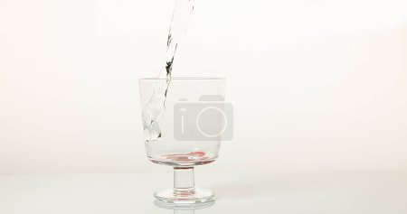Foto de Agua que se vierte en vidrio contra fondo blanco, rojo en la parte inferior del vidrio - Imagen libre de derechos