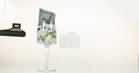 Téléchargez les photos : Verre rempli de capsules et de dollars explosant sur fond blanc - en image libre de droit