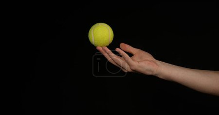 Téléchargez les photos : Main de femme lançant une balle de tennis sur fond noir - en image libre de droit