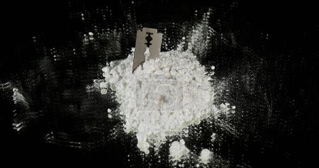Téléchargez les photos : Drogue en poudre tombant sur la lame de rasoir et les seringues sur fond noir - en image libre de droit