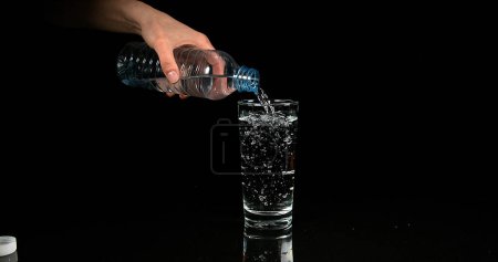 Téléchargez les photos : L'eau étant versée dans le verre sur fond noir - en image libre de droit