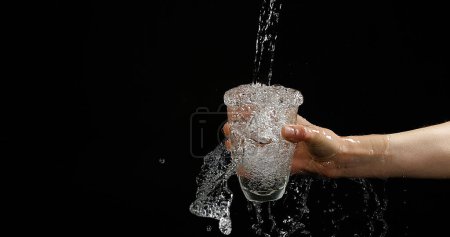 Foto de Manos de mujer y agua fluyendo en vidrio sobre fondo negro - Imagen libre de derechos