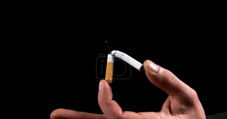 Foto de Mano del hombre que rompe un cigarrillo sobre fondo negro - Imagen libre de derechos