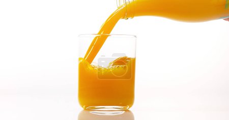 Foto de Zumo de naranja que se vierte en vidrio contra fondo blanco - Imagen libre de derechos